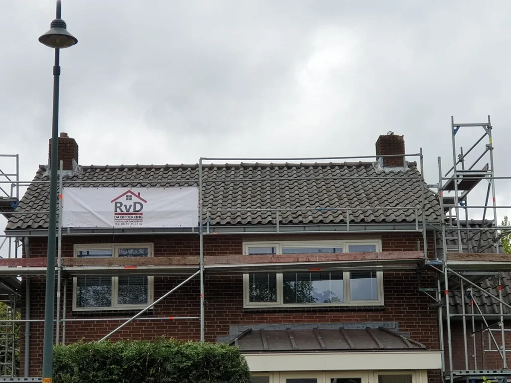 Pannendak in renovatie met steiger en het spandoek van RVD Dakbedekking