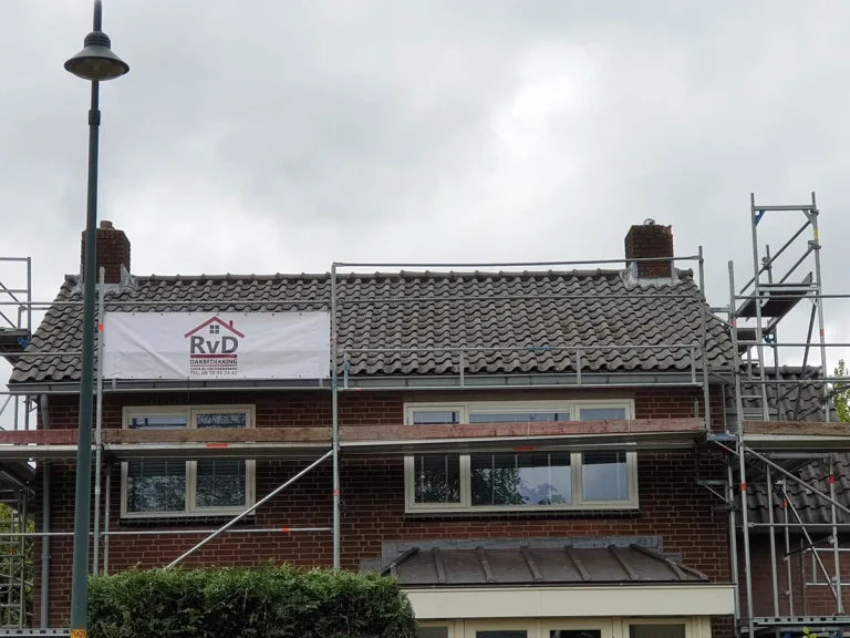 Pannendak in renovatie met steiger en het spandoek van RVD Dakbedekking